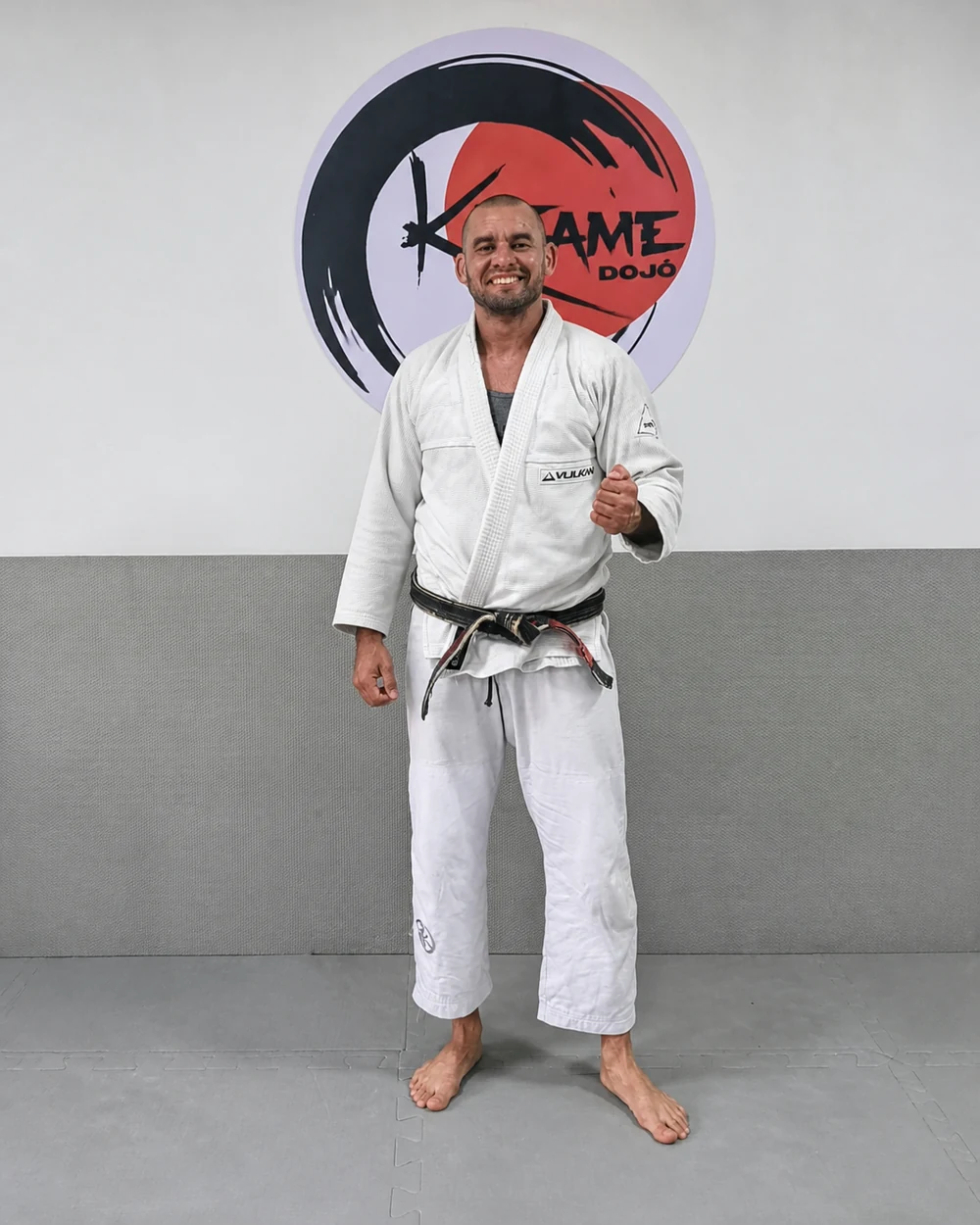Professor Leonardo Defaveri de kimono diante do emblema da Equipe Katame
